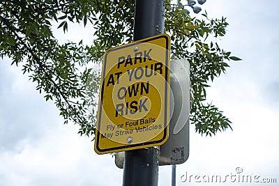 Low angle view of a Park At Your Own Risk sign outside of a baseball field, warning anyone parking their cars of the chance of fly Stock Photo