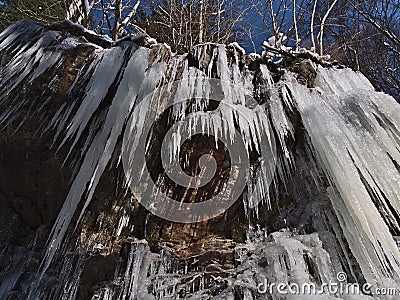 Rocky overhang on a steep slope with big frozen icicles hanging down on cold winter day at Todtnauer WasserfÃ¤lle near Todtnau. Stock Photo