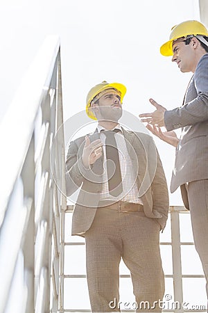 Low angle view of young male businessmen in hard hats having discussion on stairway against clear sky Stock Photo