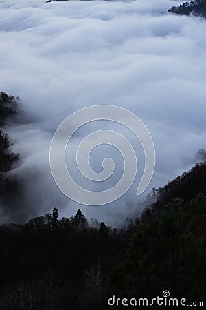 Low clouds, view of winter forest and mountains from observation deck, vertical picture of amazing natural phenomenon. Beautiful Stock Photo