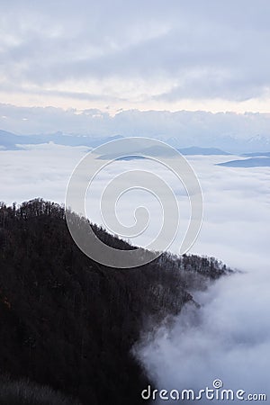 Low clouds, view of winter forest and mountains from observation deck, vertical picture of amazing natural phenomenon. Beautiful Stock Photo