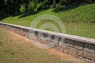 Low granite block retaining wall in an urban park, green grass and trees Stock Photo