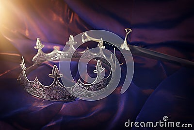 Low key image of beautiful queen/king crown and sword over dark royal purple delicate silk. fantasy medieval period Stock Photo