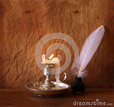 Low key image of white Feather, inkwell and burning candle on a wooden table Stock Photo