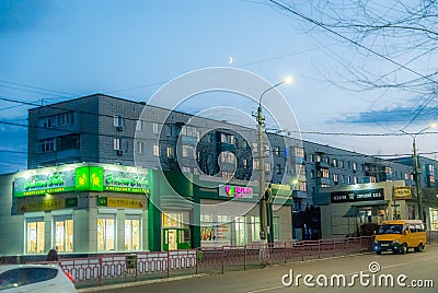 Low residential buildings, shops are closing, a lonely minibus.Dark sky, glowing advertising. In the city. Editorial Stock Photo