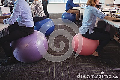 Low section of business people sitting on exercise balls while working at office Stock Photo