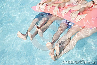 Low section of four friends in a pool holding onto an inflatable raft with feet sticking out of the water Stock Photo