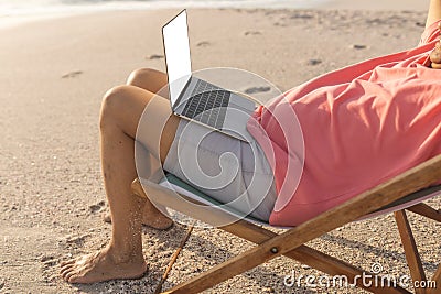 Low section of relaxed senior biracial man sitting with laptop on folding chair at beach Stock Photo