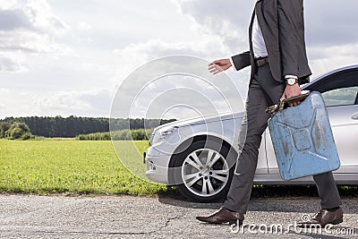 Low section of young businessman with gas can walking by broken down car at countryside Stock Photo