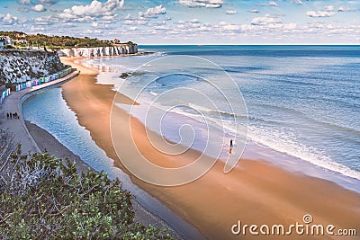 Low tide at Stone Bay, Broadstairs, Kent as summer turns to autumn, a lone surfer walks on the beach and a family on Editorial Stock Photo