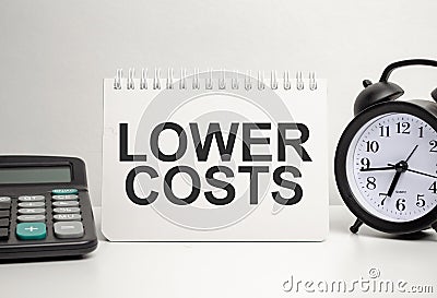 lOWER COSTS words with calculator and clock with notebook Stock Photo