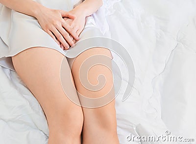 Lower part of female body wearing white Sleepwear lying on bed hand catch the crotch with copy space Stock Photo