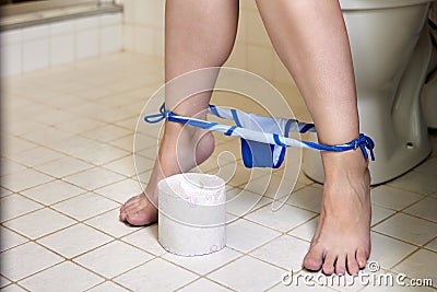 Womens legs with panties deflated in front of toilet bowl and roll of paper on floor of lavatory. Stock Photo