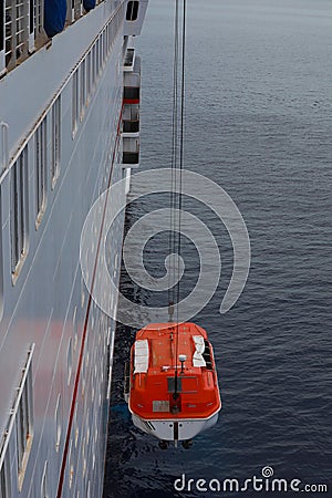 Lowering orange totally enclosed lifeboat to water. Editorial Stock Photo