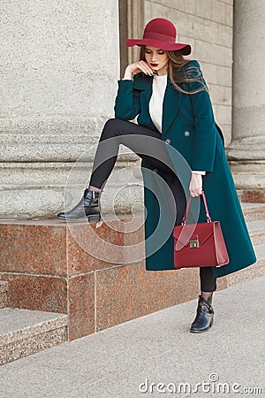 Lucky fashion girl. In hat with large fields, long warm coat, a white sweater and a lady`s leather purse. Stock Photo