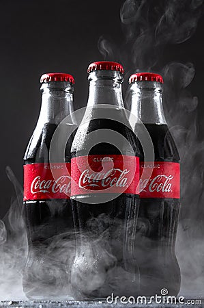 Lugansk, Ukraine - July 25, 2021: Coca Cola in glass bottles with water drops condensate and frozen smoke on dark Editorial Stock Photo