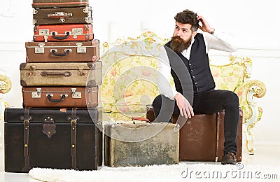 Luggage and relocation concept. Macho elegant on tired face sits, exhausted at end of packing, near pile of vintage Stock Photo