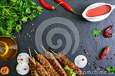 Lula kebab is a traditional Arabic dish. Meat shashlik on wooden skewers, spicy tomato sauce on black background. Stock Photo