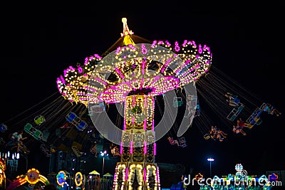 Luminous carousel turntables spin with people in the evening. Fun for kids and adults in an amusement park Editorial Stock Photo
