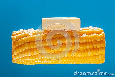 A lump of butter is melted on hot cooked corn. A large ear of yellow corn is shown against a light blue background Stock Photo