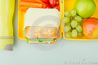 Lunch box with vegetable sandwich, cherry tomatoes, grapes, green apple, pear, bottle on a wooden blue table. Stock Photo