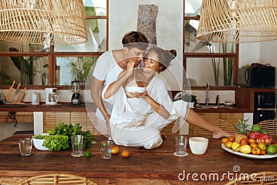 Lunch. Couple Cooking At Kitchen On Romantic Weekend. Beautiful Woman Sitting On Wooden Table Feeding Happy Man. Stock Photo