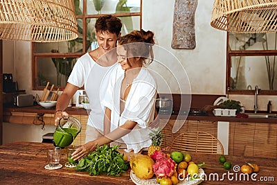 Lunch. Couple At Kitchen On Romantic Weekend. Beautiful Woman Holding Glass While Happy Man Pours Smoothie. Stock Photo