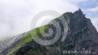 Lush green mountain landscape and mountain peak with light white clouds and a sharp cliff drop off Stock Photo