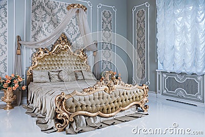 Luxury bedroom in light colors with golden furniture details. Big comfortable double royal bed in elegant classic Stock Photo