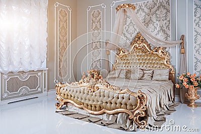 Luxury bedroom in light colors with golden furniture details. Big comfortable double royal bed in elegant classic Stock Photo