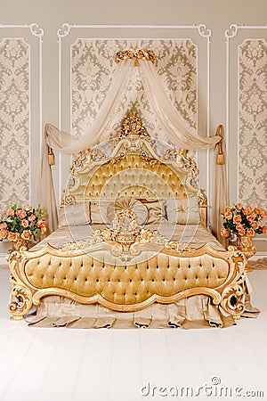 Luxury bedroom in light colors with golden furniture details. Big comfortable double royal bed in elegant classic Stock Photo