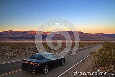 Luxury black fast American car driving on desert highway in Death Valley California, road trip, colourful sunrise mountains view Stock Photo