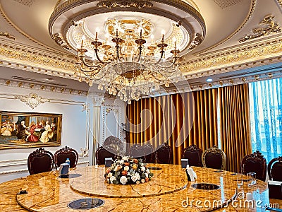 Luxury dining room interior with many shiny gold-plated details, crystal chandeliers, wooden chairs, and classic wall painting Editorial Stock Photo