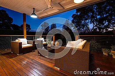 Luxury outdoor lounge area with chairs and cushions looking onto beautiful garden from a deck, shot at twilight Stock Photo