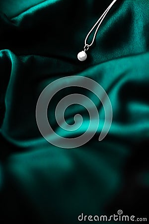 Luxury white gold pearl necklace on dark emerald green silk background, holiday glamour jewelery present Stock Photo