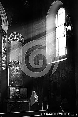 LVIV, Armenian Cathedral, UKRAINE - OCTOBER 2018:Christian woman praying. Natural sunlight shining into a medieval church. Editorial Stock Photo