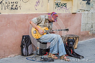 LVIV, UKRAINE - AUGUST 2016: Street musician playing rock hits of the electric guitar, sitting with a large black dog, near the wa Editorial Stock Photo