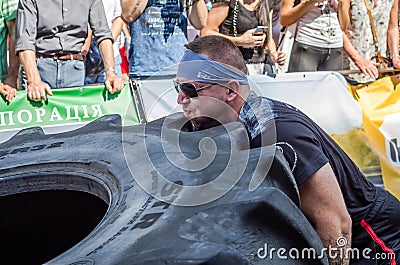 LVIV, UKRAINE - AUGUST 2017: A super strong athlete raises a huge Good year wheel at competitions in front of enthusiastic spectat Editorial Stock Photo