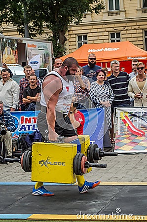 LVIV, UKRAINE - JULY 2016: Mighty strong athlete bodybuilder strongman carries heavy iron suitcases on the street in front of Editorial Stock Photo
