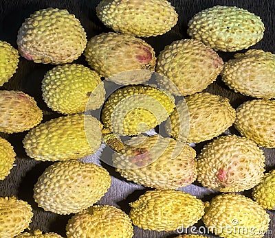 Lychee- small rounded fruit with sweet white scented flesh, a large central stone, and a thin rough skin- on brown wooden Stock Photo