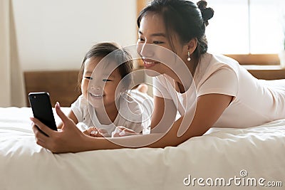 Lying in bed asian mother show daughter cartoons on cellphone Stock Photo