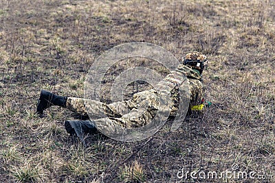 Lying Ukrainian soldier disguises in steppe against of background of dry grass Stock Photo