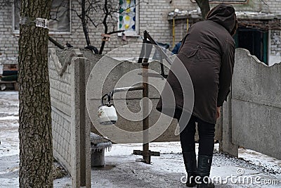Lyman, Donetsk region, Ukraine - January 2023: A woman collects water from a water column in the yard of an apartment building Editorial Stock Photo