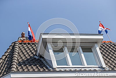 Maastricht, South Limburg, Netherlands. April 27, 2022. King`s day, man on the gabled roof with two Dutch flags Editorial Stock Photo