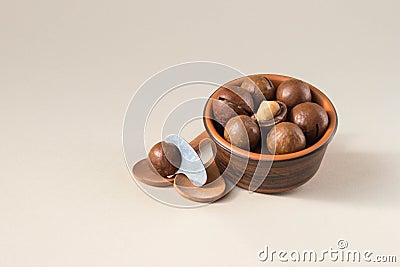 Macadamia nuts in ceramic bowl on beige background. Nuts with sawn nutshells and with opener key on the wooden spoon. Healthy Stock Photo