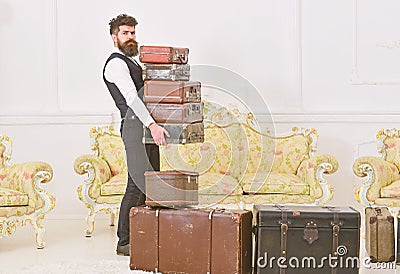 Macho, elegant porter on strict face carries pile of vintage suitcases. Butler and service concept. Man with beard and Stock Photo