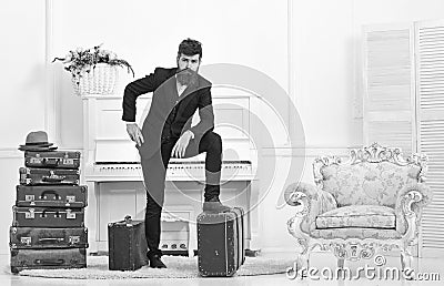 Macho elegant on thoughtful face standing near pile of vintage suitcase. Man, traveller with beard and mustache with Stock Photo