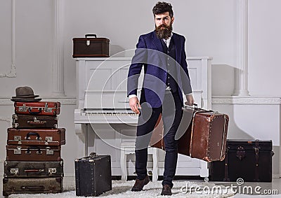 Macho stylish on strict face stands and carries big vintage suitcase. Man, traveller with beard and mustache with Stock Photo