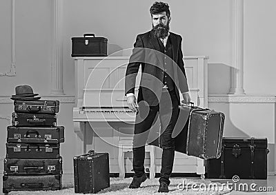 Macho stylish on strict face stands and carries big vintage suitcase. Man, traveller with beard and mustache with Stock Photo