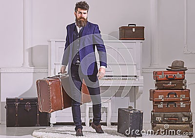 Macho stylish on strict face stands and carries big vintage suitcase. Man, traveller with beard and mustache with Stock Photo